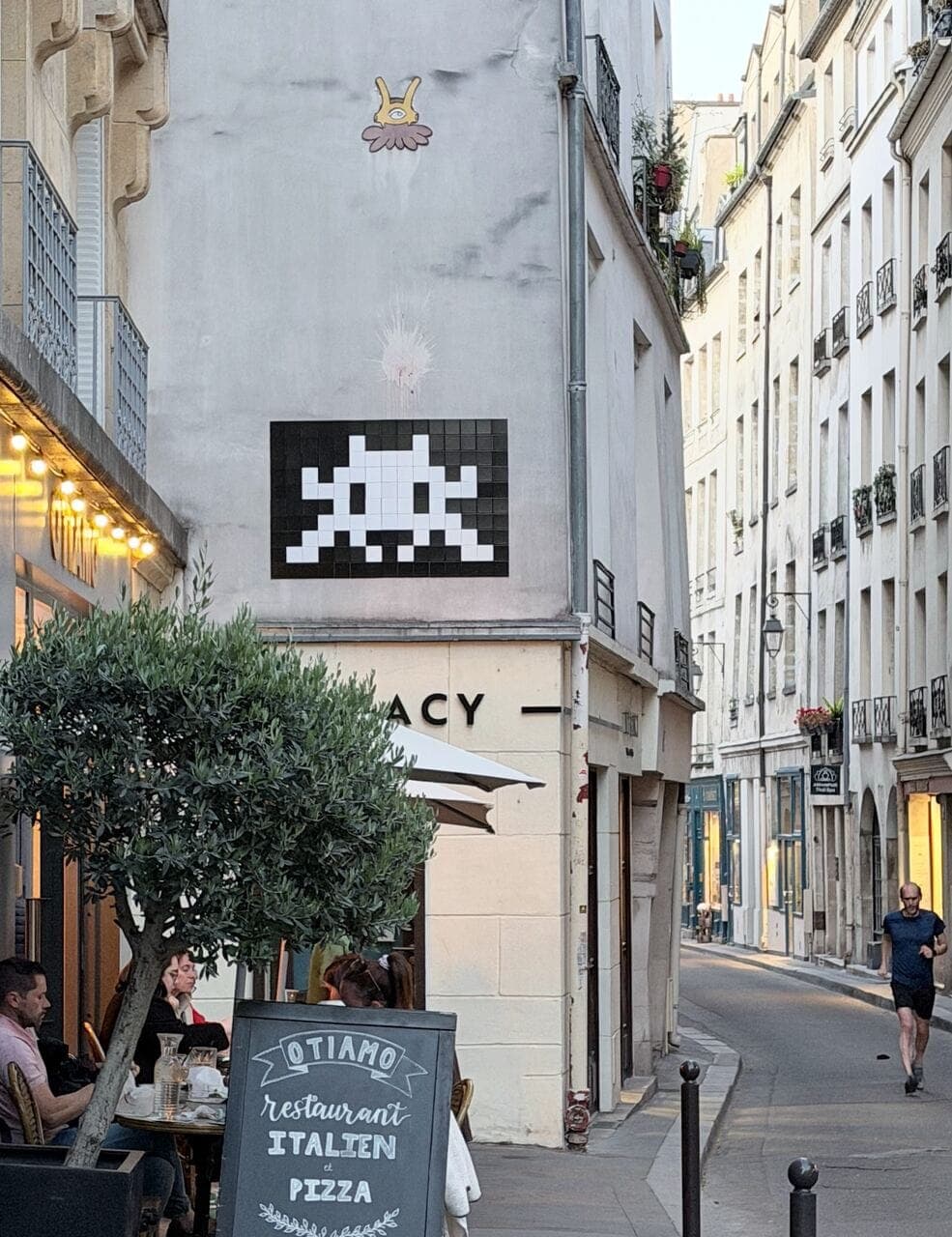 A Space Invader mosaic set high on a corner building in the Marais, Paris, above an Italian restaurant terrace