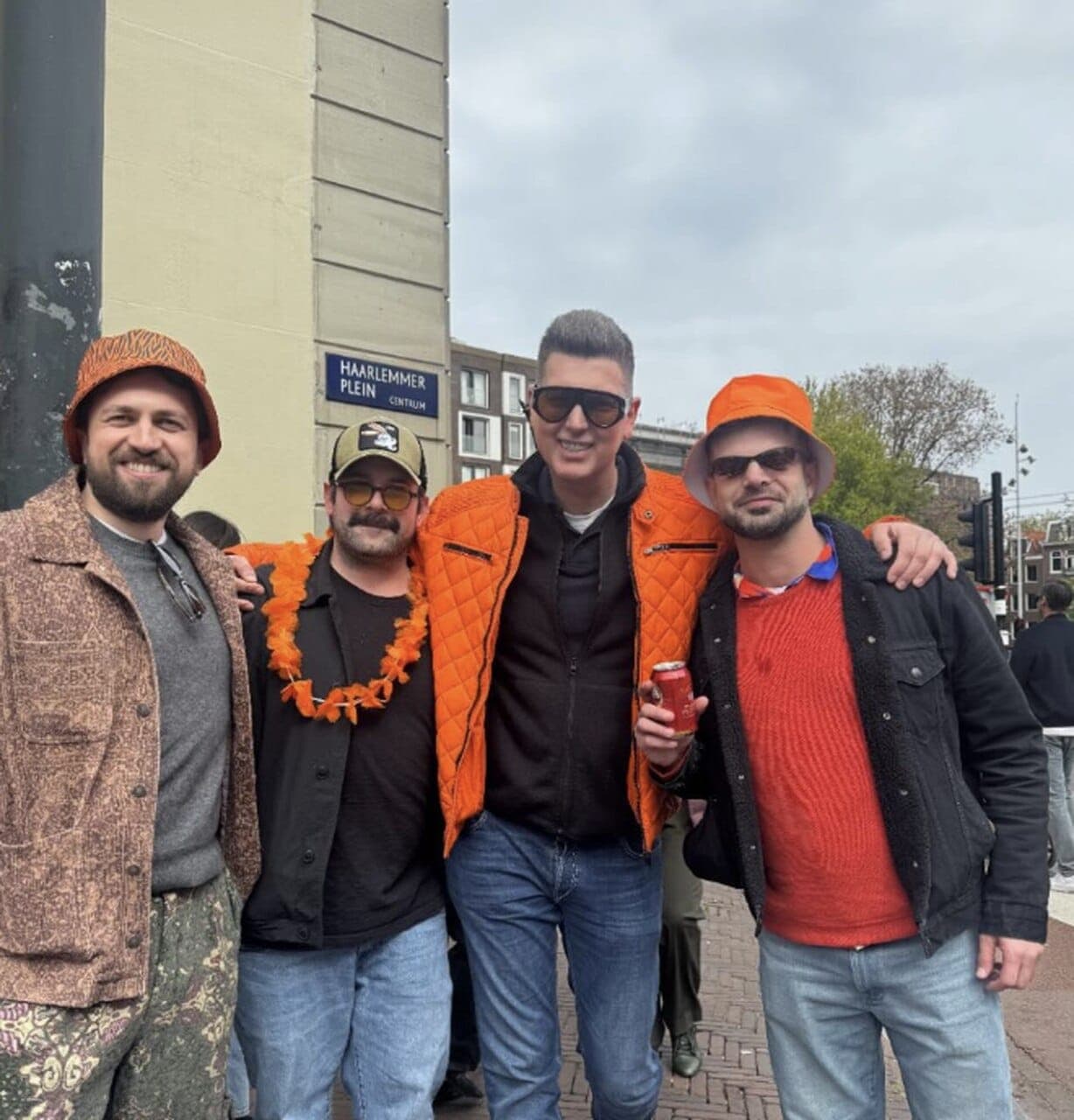 Four friends in orange King's Day outfits by the Haarlemmerplein street sign in Amsterdam