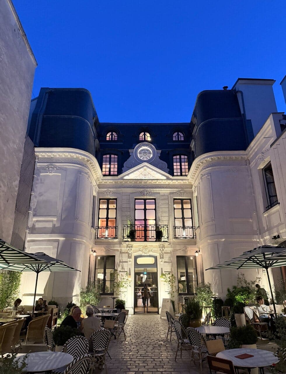The courtyard of Locke hotel in Paris at blue hour, café tables and parasols set out below a floodlit Haussmann facade