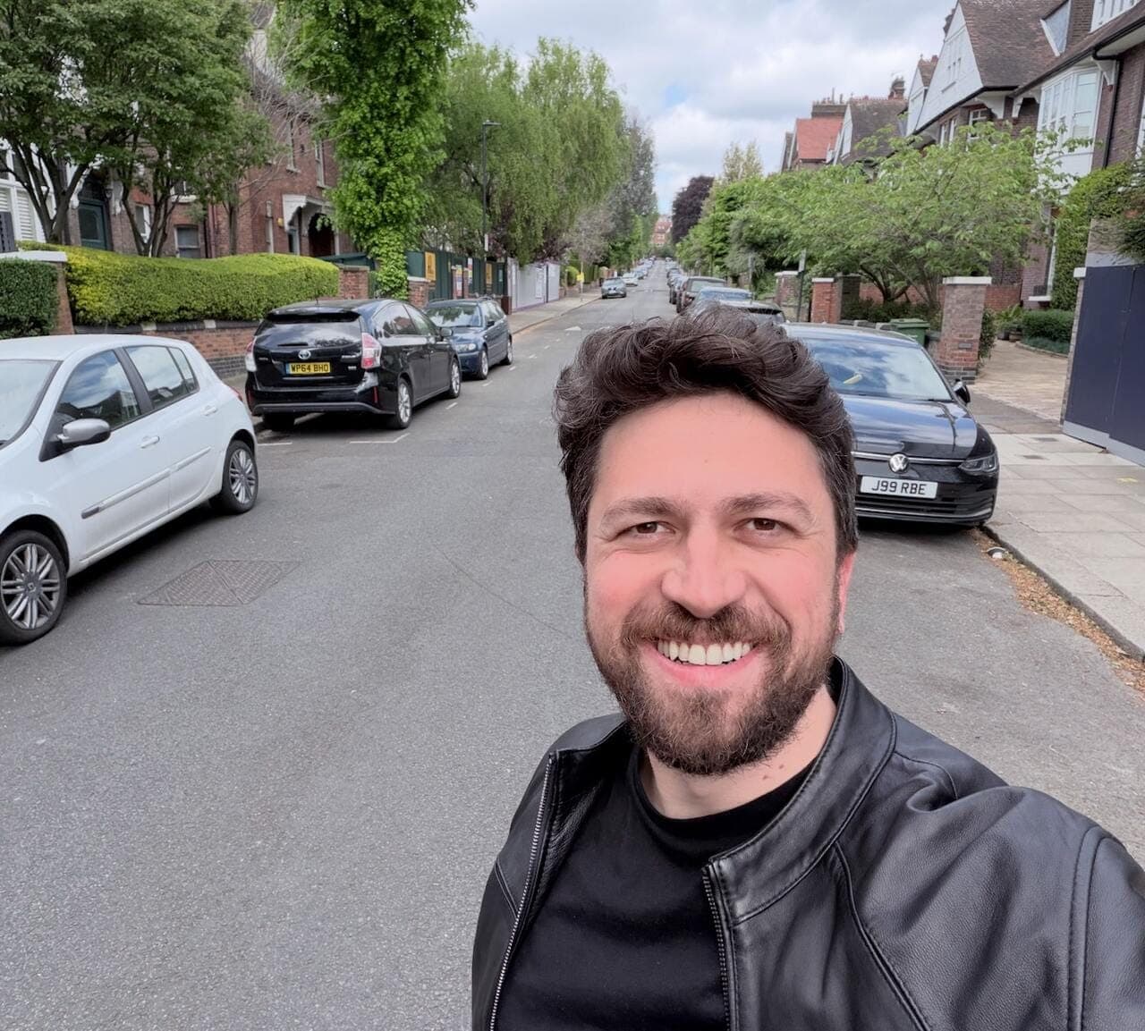 Emre Elbeyoglu taking a selfie on a tree-lined residential street in London