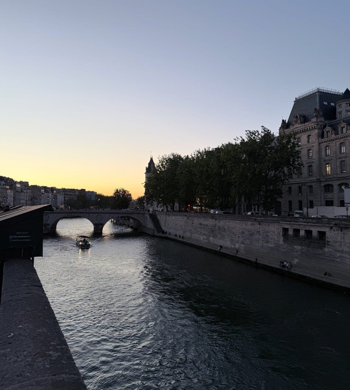 Golden hour on the Seine in Paris, a small boat passing under a stone bridge