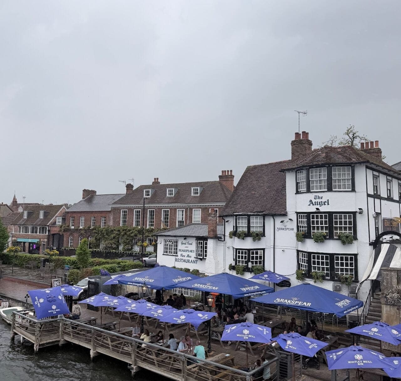 The Angel on the Bridge pub at Henley-on-Thames, its riverside terrace lined with blue parasols under grey sky